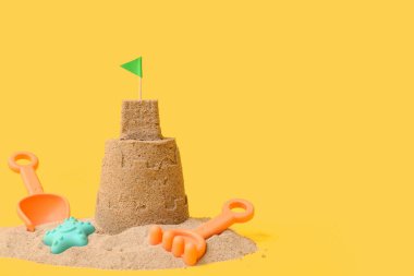 Güzel kumdan kale, sarı arka planda plaj oyuncakları.