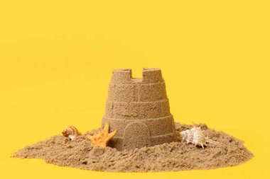 Sarı arka planda deniz yıldızı ve deniz kabukları olan güzel bir kumdan kale.