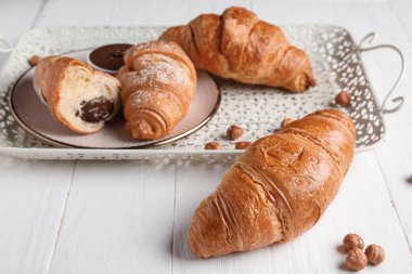 Çikolatalı kruvasan ve beyaz ahşap arka planda fındıklı tepsi.