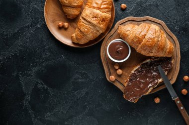 Çikolata kaplı tatlı kruvasanlar ve siyah arka planda fındıklar.