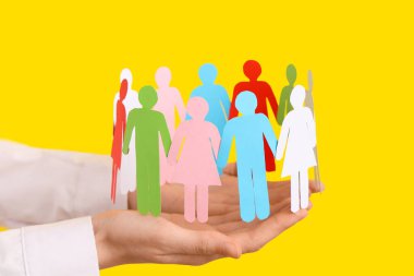 Sarı arka planda kağıt insan figürleri olan kadın eller, yakın plan. Çeşitlilik ve kapsama kavramı