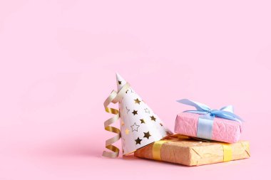 Hediye kutularıyla parti şapkası ve pembe arka planda konfeti.