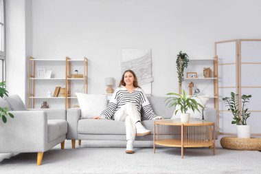 Oturma odasındaki gri kanepede oturan genç kadın.