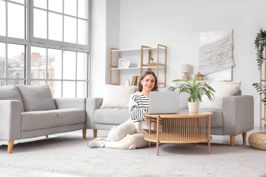 Oturma odasındaki masada dizüstü bilgisayar kullanan genç kadın.