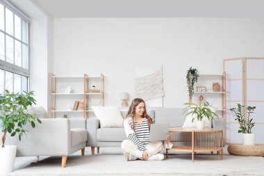 Oturma odasında dizüstü bilgisayar kullanan genç bir kadın.