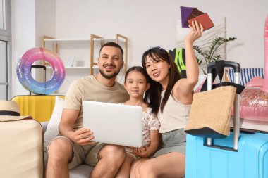 Evde dizüstü bilgisayar kullanan seyahat aksesuarlı mutlu bir aile.