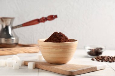 Bir kase kahve tozu, fasulye, şeker küpleri ve beyaz fayans masasının üzerinde de kahve.