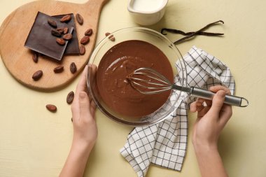 Kadın elleri bej arka planda erimiş çikolata çırpıyor. Üst görünüm