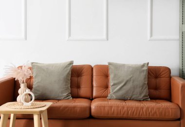 Oturma odasındaki ışıklı duvarın yanındaki yastıklı kahverengi kanepe.