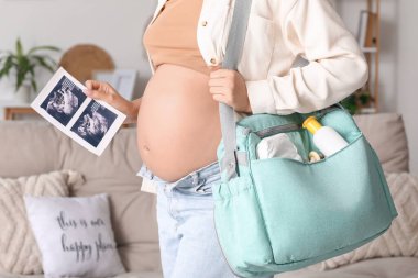 Evde sonogram görüntüsü ve doğum çantası olan hamile bir kadın var.