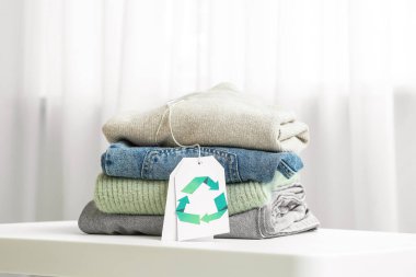 Beyaz masa üzerinde geri dönüşüm logosu olan kıyafet yığını ve etiket