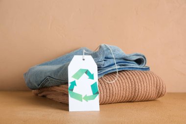 Bej arka planda geri dönüşüm logosuna sahip kıyafet yığını ve etiket