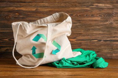 Geri dönüşüm logosu ve ahşap arka planda giysileri olan çanta.