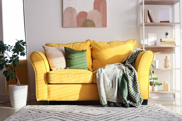 Interior of stylish room with comfortable yellow sofa, mirror and shelving unit