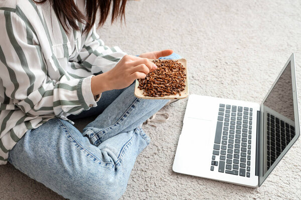 Молодая женщина с жареными насекомыми и ноутбуком сидит дома на ковре