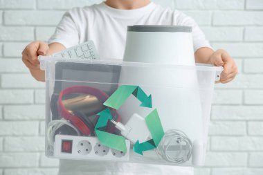 Beyaz tuğla arka planda geri dönüşüm için elektronik atık taşıyan kadın, yakın plan