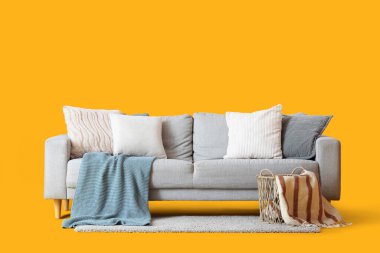 Yastıklı rahat gri kanepe, hasır sepet ve sarı arka planda battaniyeler.