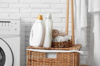 Çamaşır odasında çamaşır makinesinin yanında çamaşır sepeti ve şişe deterjan var.