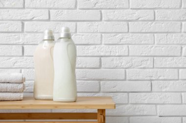 Beyaz tuğla duvarın yanında çamaşır deterjanı şişeleri ve havlular olan ahşap bir bank.