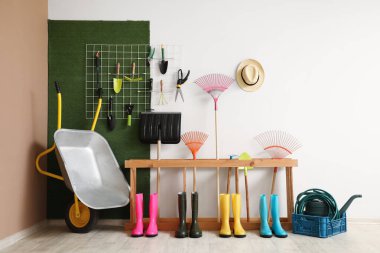 Çizmeler ve bahçe aletleri ile ahır renkli duvar yakınında durmak