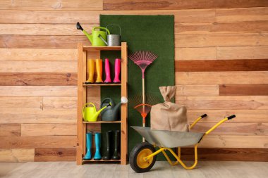 Bahçe aletleri ile raf ünitesi ve ahır ahşap duvarın yanındaki el arabasında çuval
