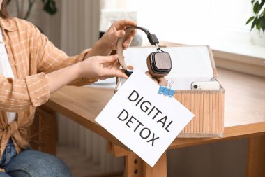 Kadın kulaklığı kutuya ve kağıda koyup evde dijital detoks yapıyor, yakın plan. Ulusal Fişi Çıkarma Günü