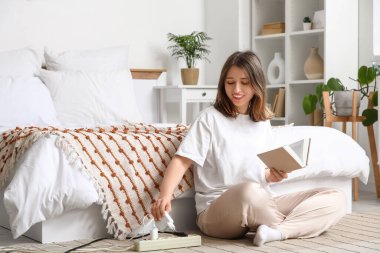 Kitaplı genç bir kadın yatak odasında şarj aletini çıkarıyor. Ulusal Fişi Çıkarma Günü