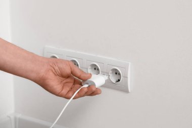 Erkek el şarj aletini yuvadan çıkarıp evdeki ışık duvarına takıyor.