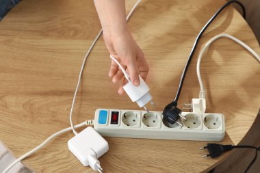 Kadın el, uzatma kablosundan şarj aletini çıkarıyor. Masanın üstünde. Ulusal Fişi Çıkarma Günü