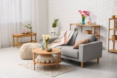 Şenlikli oturma odasının içinde şık gri kanepe, ahşap sehpa ve Paskalya süslemeleri var.