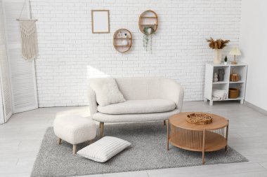 Beyaz çatı katı tarzı oturma odasının içinde rahat kanepe, puf ve kahve masası var.