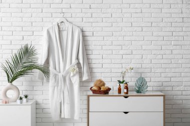 Duvarda asılı beyaz bornoz ve banyodaki çekmecelerde farklı banyo malzemeleri.