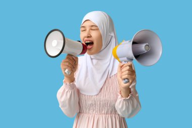 Genç Asyalı Müslüman kadın mavi arka planda megafonlara bağırıyor. Ulusal Duyulma Günü