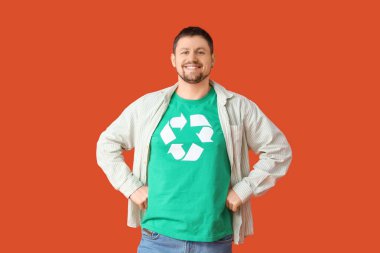 Turuncu arka planda geri dönüşüm logosu olan tişörtlü mutlu genç adam. Ekoloji kavramı
