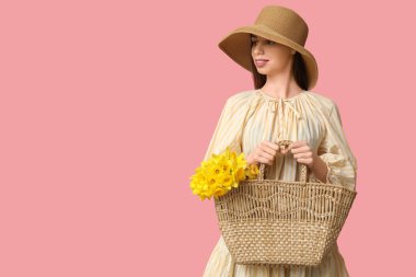 Güzel, genç, mutlu bir kadın pembe arka planda narsisli çiçeklerle dolu bir çanta taşıyor.