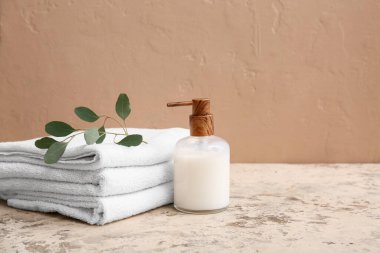 Temiz yumuşak havlu yığını, bir şişe kozmetik ürünü ve kahverengi duvarın yanında bitki.