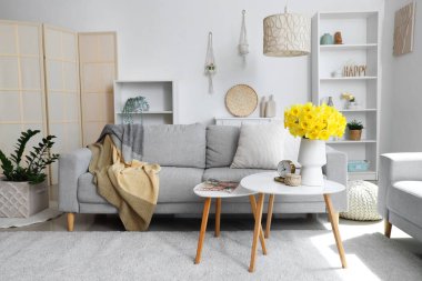 Yumuşak kanepe, kahve masası ve açık oturma odasında narsisli çiçekler.