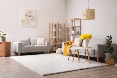 Konforlu kanepeler, raf ünitesi ve oturma odasında vazo dolusu narsist çiçekli kahve masası.