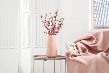 Işık odasındaki koltuğun yanındaki kahve masasında Sakura çiçekli vazo.