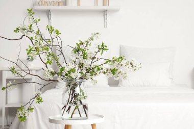 Sehpanın üzerinde çiçek açan bir vazo beyaz şık bir yatak odasında, rahat bir yatağın yanında, yakın plan.