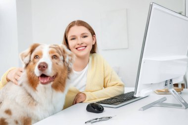 Genç kadın ve şirin Avustralyalı çoban köpeği ana ofiste bilgisayarla masada oturuyor.