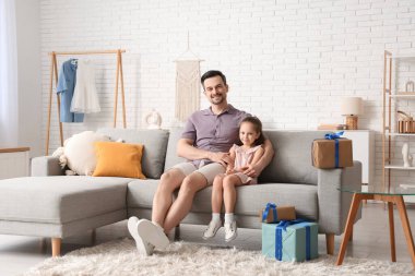 Baba ve kızı kanepede oturuyor ve hediye kutularının yanında sarılıyorlar. Babalar günü kutlaması.