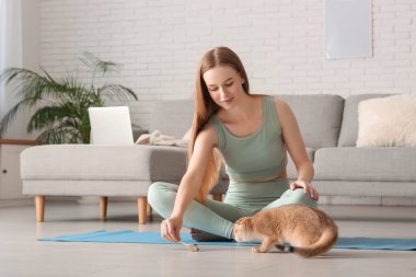 Evde yoga minderinde kedi yavrusuyla oynayan genç bir kadın.