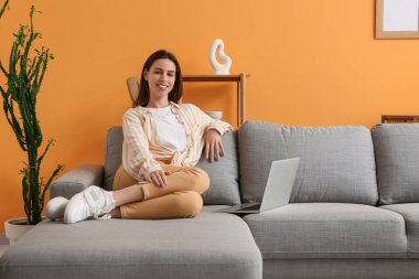 Genç bir kadın güzel oturma odasında dizüstü bilgisayarla kanepede oturuyor.