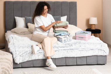 Güzel, genç, mutlu, Afro-Amerikan bir kadın yatak odasında temiz giysiler katlıyor.