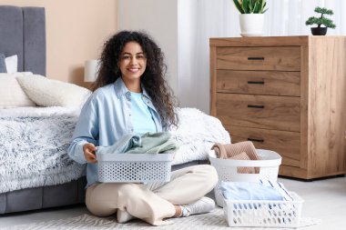 Güzel, genç, mutlu, Afro-Amerikan bir kadın. Elinde sepetler, temiz giysileri katlıyor.