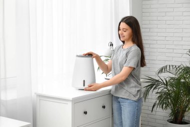 Genç bir kadın modern nemlendiriciyi açıyor. Odadaki çekmecelerin üzerinde.