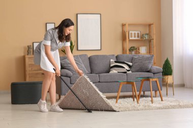 Oda hizmetçisi odayı halının altına süpürüyor.