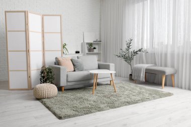 Katlanır ekran, gri kanepe, bank ve sehpası olan şık bir oturma odası.