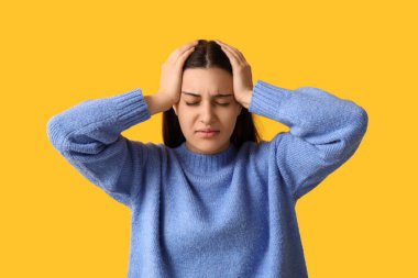 Sarı arka planda baş ağrısı çeken güzel bir genç kadın.